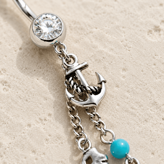 Silver belly button ring with anchor charm and turquoise bead on beige sand background