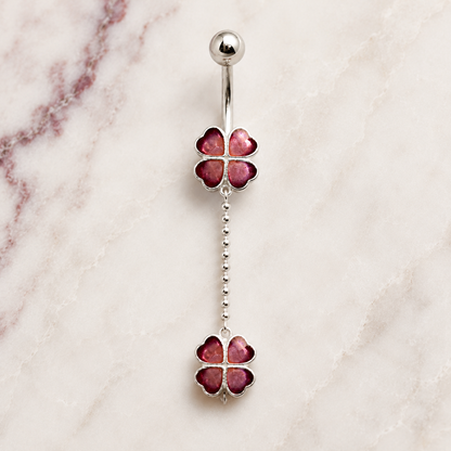 Silver belly button ring with red clover-shaped stones on a marble background