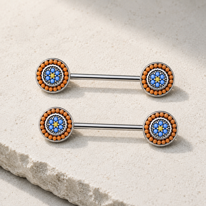 Two metallic nipple barbells with blue and orange bead designs on a stone surface.