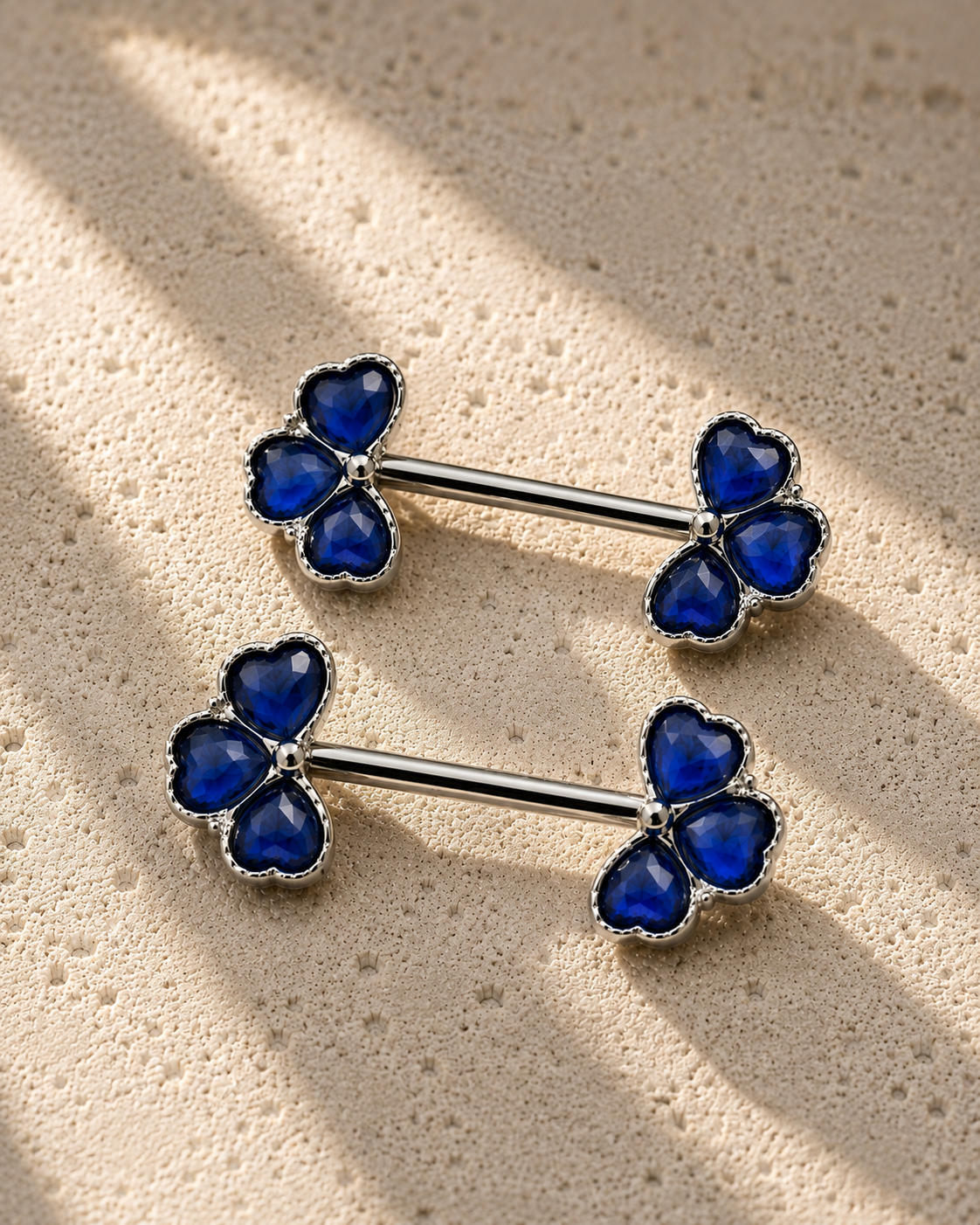 nipple bars with blue gemstones on a beige surface