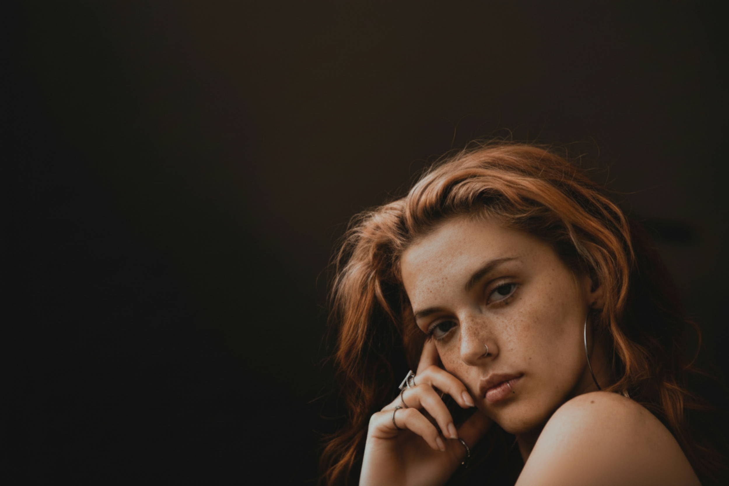 Close-up of a woman with red hair and freckles, wearing hoop earrings and rings.