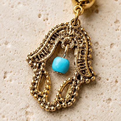 Close up of hamsa dangle with turquoise press fit stone and bead, antique gold carvings navel ring detail
