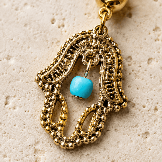 Close up of hamsa dangle with turquoise press fit stone and bead, antique gold carvings navel ring detail
