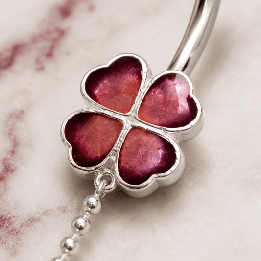 Silver four-leaf clover charm with pink gemstones on a marble background