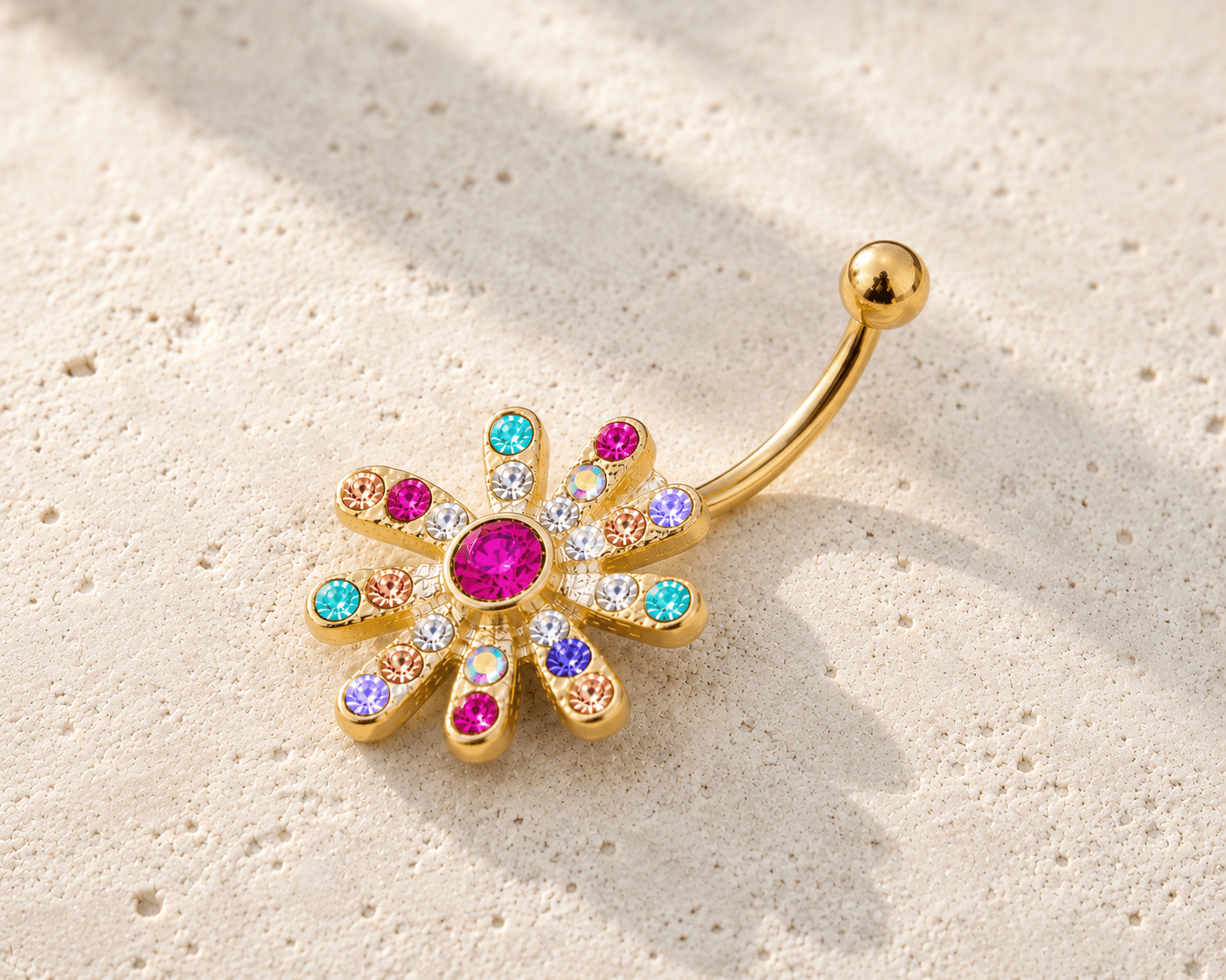 Gold belly button ring with colorful gemstones on a beige background