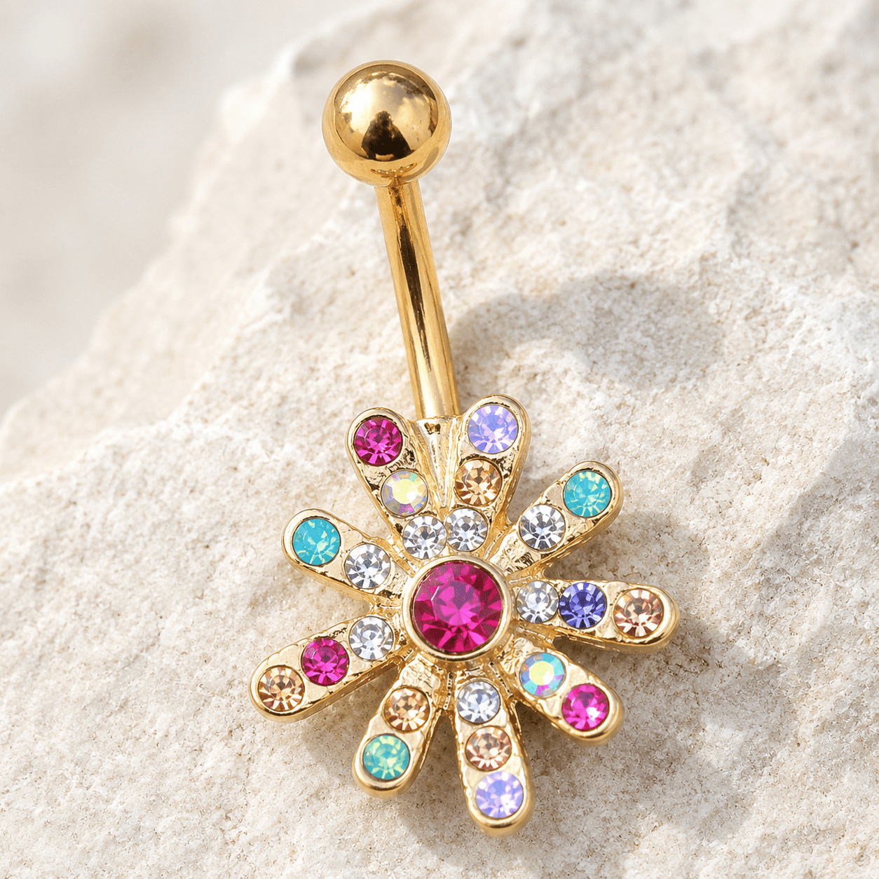 Gold belly button ring with colorful gemstones on a textured beige surface