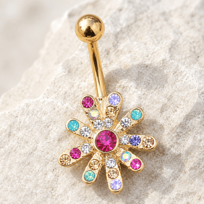 Gold belly button ring with colorful gemstones on a textured beige surface