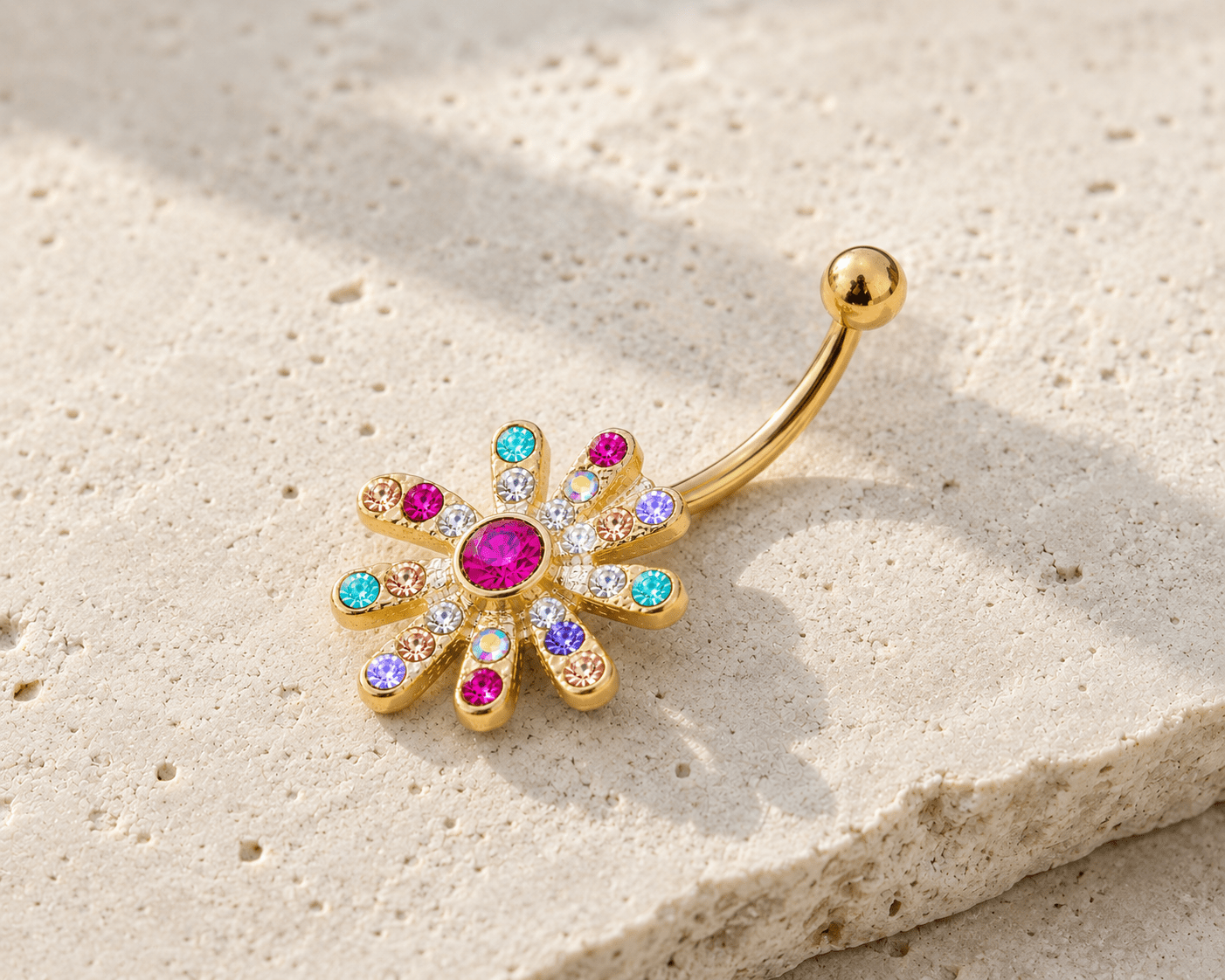 Gold belly button ring with colorful gemstones on a beige stone surface