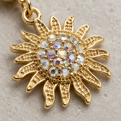 A gold sunburst pendant charm with a central cluster of iridescent round rhinestones, shown close-up on a textured light gray surface.