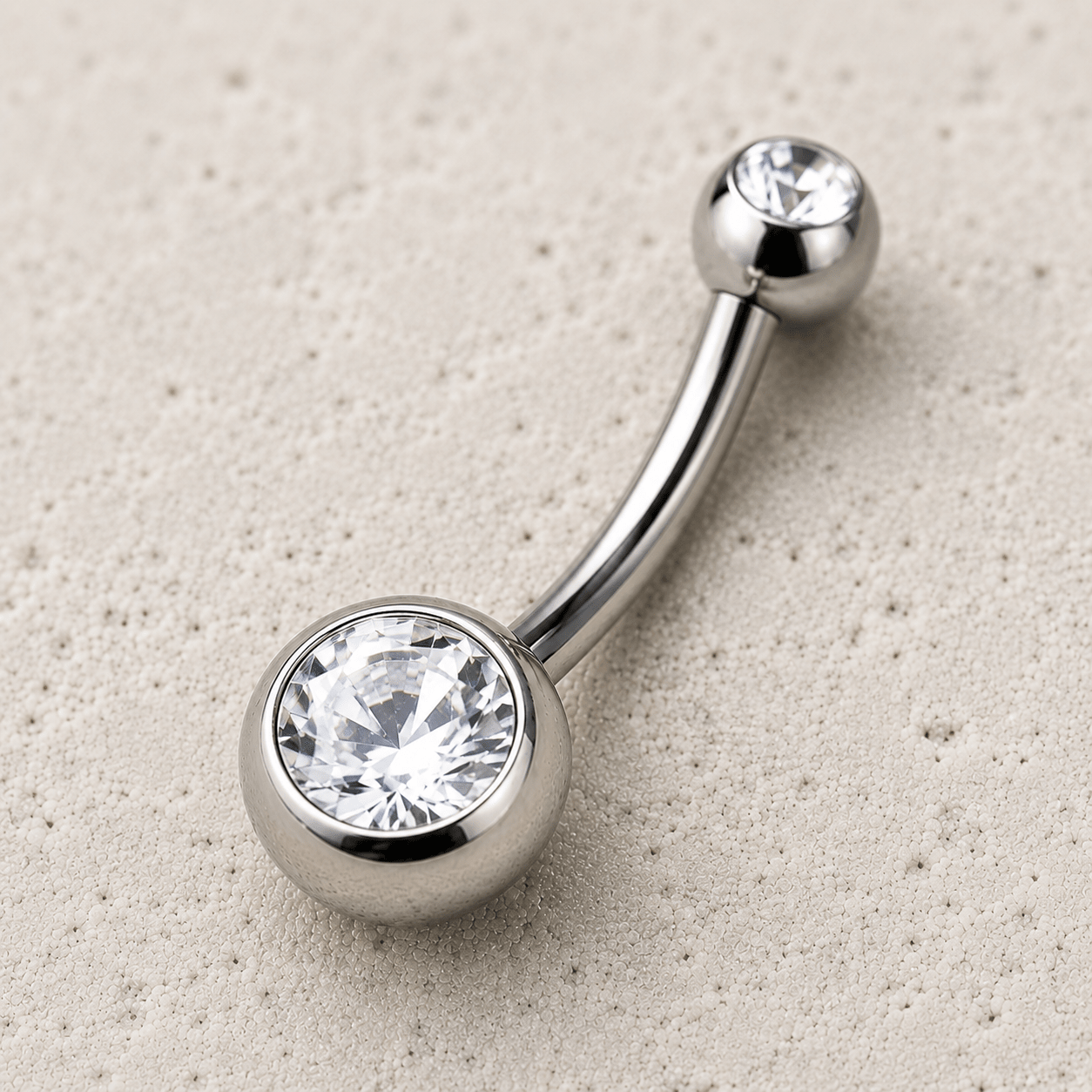 Silver belly button ring with clear gemstones on a beige background