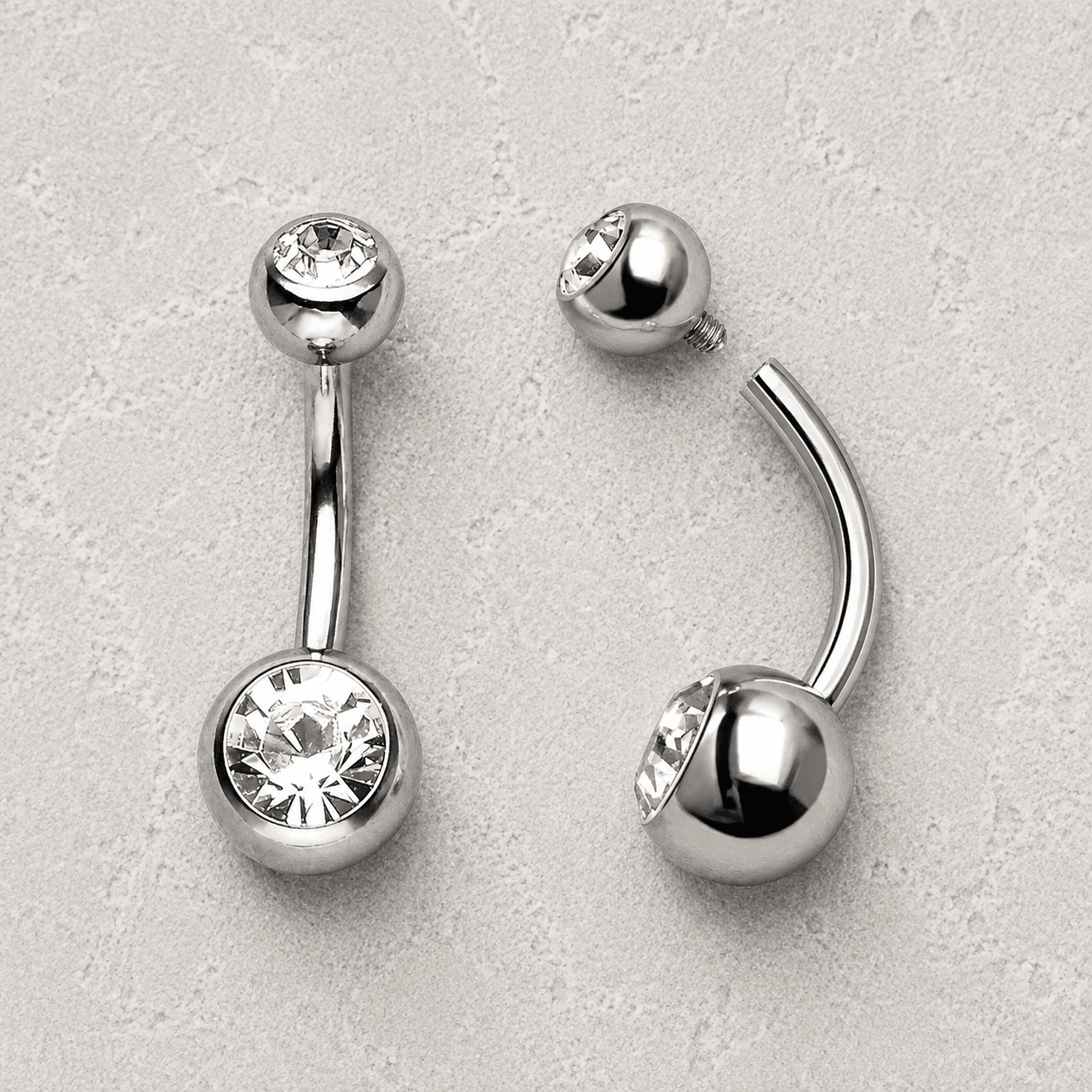 Silver belly button rings with clear gemstones on a light gray background