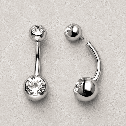 Silver belly button rings with clear gemstones on a light gray background