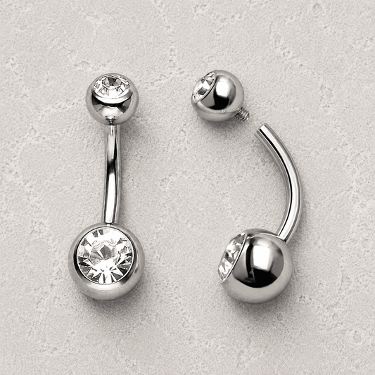 Silver belly button rings with clear gemstones on a light gray background