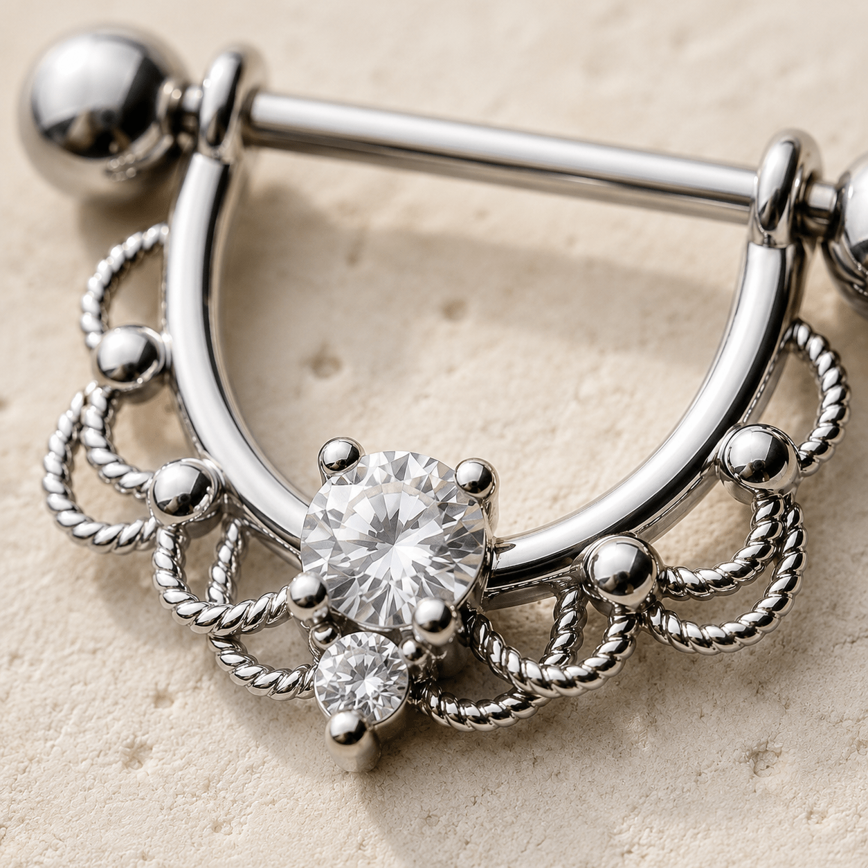 Close up of filigree design and two prong set clear CZ on nipple ring, mirror finish detail