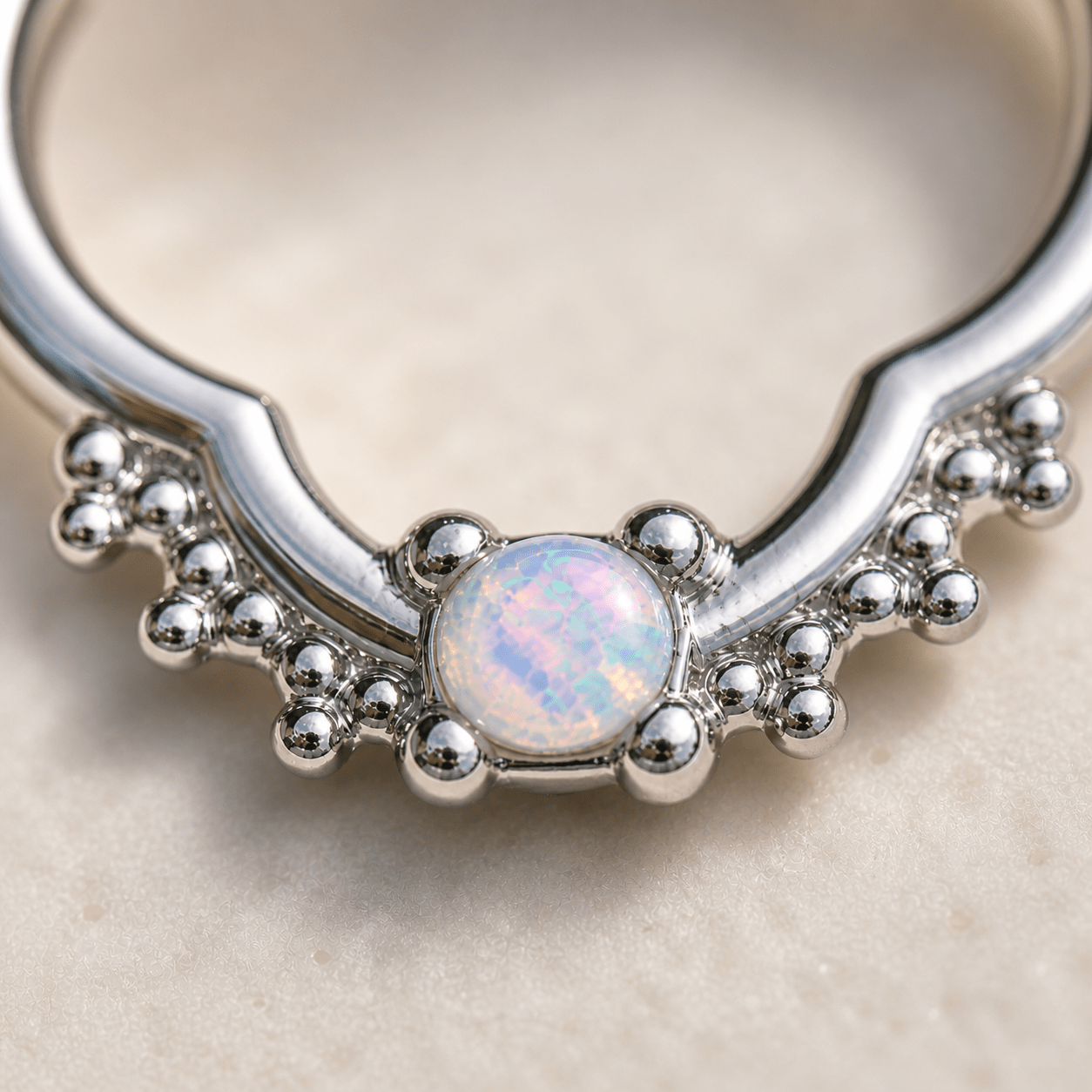 Close up of white synthetic opal in ornate quatrefoil design, 316L stainless steel captive bead ring detail