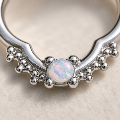 Close up of white synthetic opal in ornate quatrefoil design, 316L stainless steel captive bead ring detail