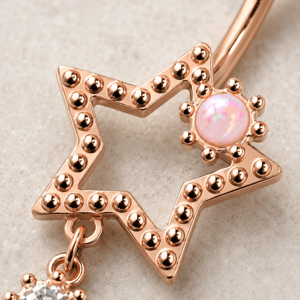 Close up of white synthetic opal large star and dangling clear CZ star on rose gold navel ring detail