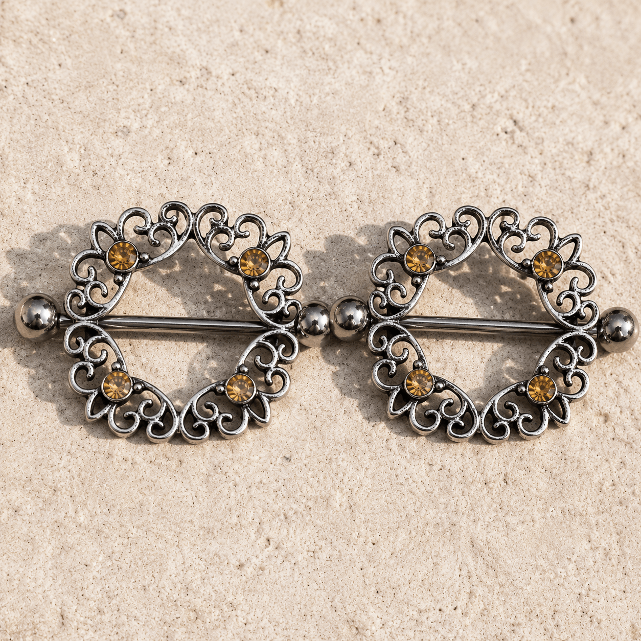 Styled aesthetic flat lay of topaz CZ ornate nipple shield pair, warm amber gemstone body jewelry 316L stainless steel