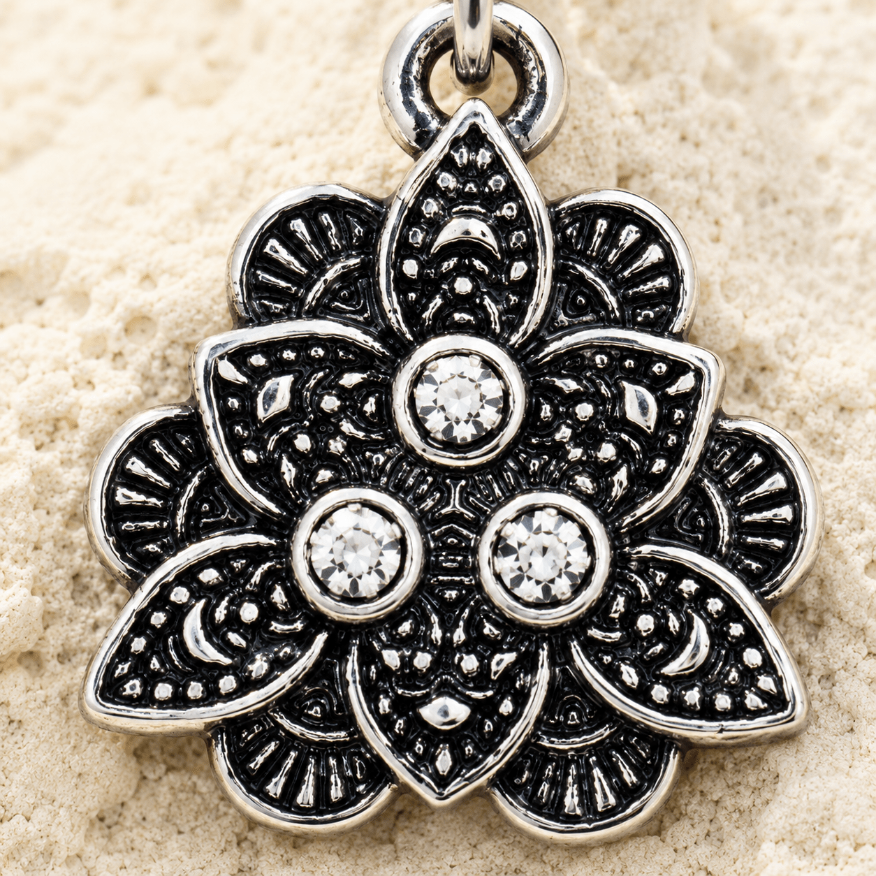 Silver floral belly button ring with gemstones on a beige sand background