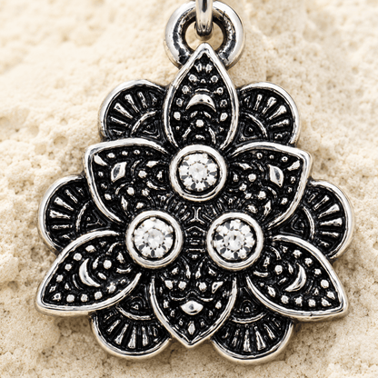 Silver floral belly button ring with gemstones on a beige sand background