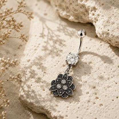 Silver belly button ring with floral pendant on beige stone surface
