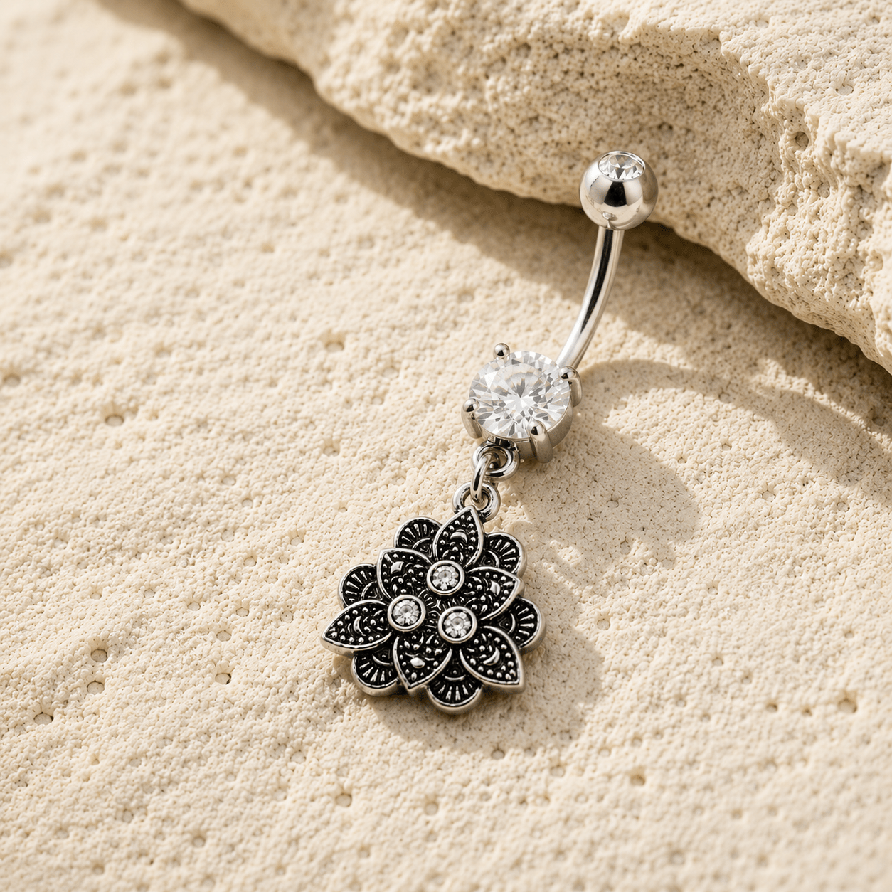 Silver belly button ring with floral pendant on beige sand