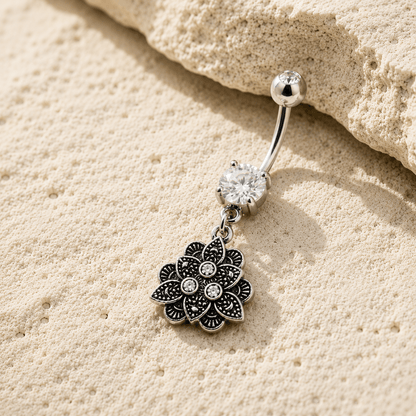 Silver belly button ring with floral pendant on beige sand