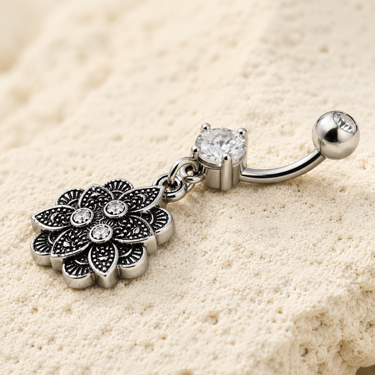 Silver belly button ring with floral design and gemstones on a beige background