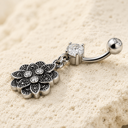 Silver belly button ring with floral design and gemstones on a beige background