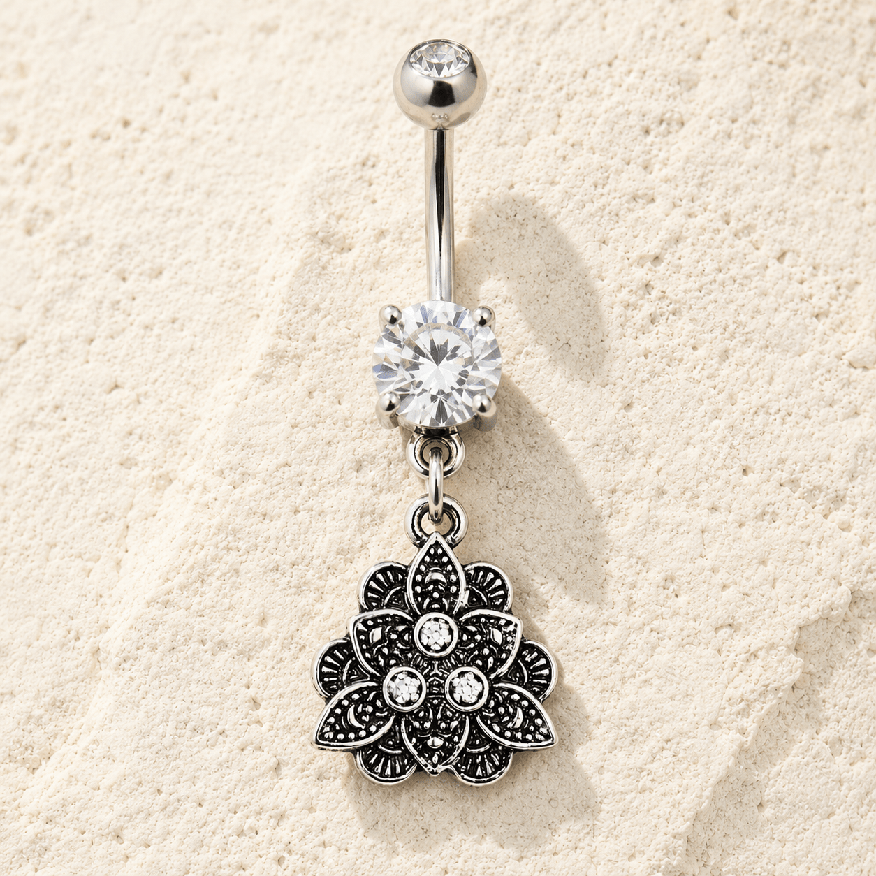 Silver belly button ring with floral pendant on a beige sand background